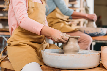 Obraz na płótnie Canvas cropped view of teacher and child making ceramic pots on pottery wheels