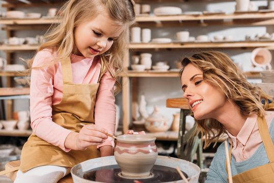 mother and daughter painting ceramic pot in pottery workshop