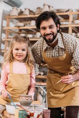 smiling teacher and happy child painting ceramic pot on pottery class teacher
