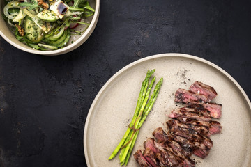 Traditional barbecue skirt steak sliced with green asparagus and salad as close-up on a plate