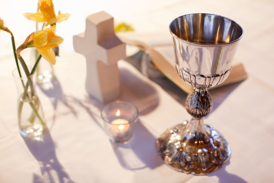 Abendmahlskelch, Kreuz, Kerze, Bibel und Osterglocken auf einem weißen Tischtuch