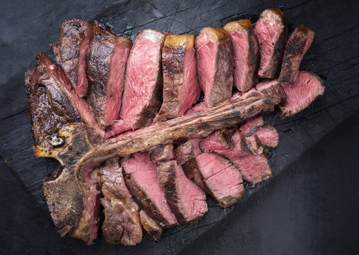 Barbecue dry aged wagyu porterhouse steak sliced as top view on a burnt board