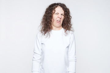 Stylish young female clenches teeth, has disgusting expression, refuses do something, makes grimace, isolated over white background. Dissatisfied youngster in casual white feels averse to do something - obrazy, fototapety, plakaty
