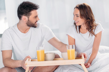 young man brought breakfast in bed for smiling girlfriend