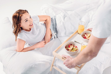 Obraz na płótnie Canvas partial view of man brought breakfast in bed for smiling girlfriend