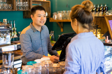 Positive confident cashier taking customers order and asking about preferences. Smiling handsome young staff friendly talking to client. Coffee shop company concept