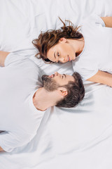 overhead view of young couple in love looking at each other while lying on bed together