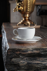 Cup of tea stands on a rough wooden surface of the table against the background of an ancient samovar