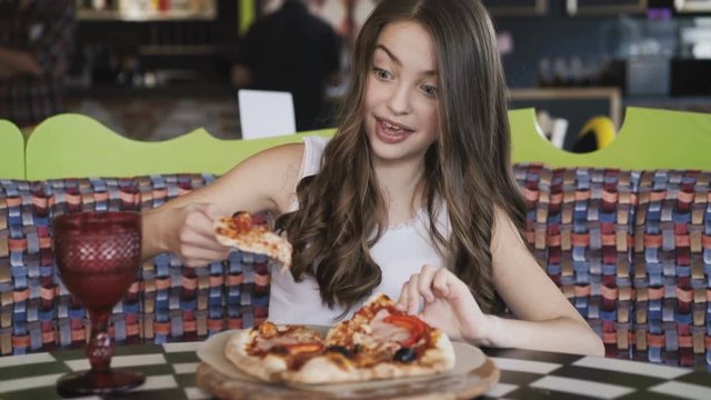 Pretty young girl eating pizza with enjoy in cafe. 4K