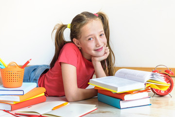 Homeschooling. The child, the pupil, the schoolgirl lies on a floor with a pile of books and writes homework. Education of children. Training of children in kindergartens and schools.