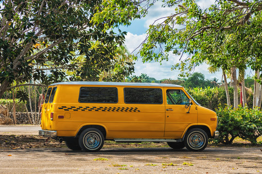 Picture of yellow classic taxi van between green trees