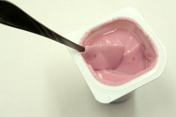 strawberry yogurt in white plastic cup on wooden white background. strawberry yoghurt. pink yogurt.