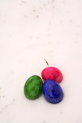 Drei bunte Ostereier in verschneiter Wiese. Hochformat.