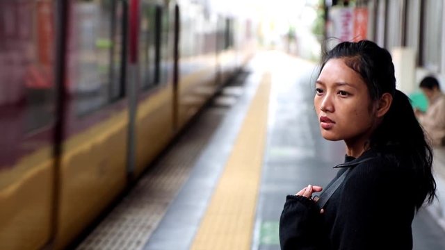 The woman is waiting at the station of the train station to take the train. The train does not stop at the station where waiting people. Girl watches the train on the tracks.
