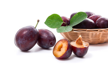 Yellow wooden basket with ripe plums, whole and half ripe plums isolated on a white background..