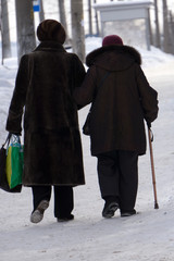 Two elderly ladies are strolling around the city on cold winter day wearing stylish clothes and holding each other under hand .
