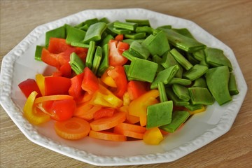 fresh, sliced vegetables, carrots, paprika and green grass beans in a white saucer