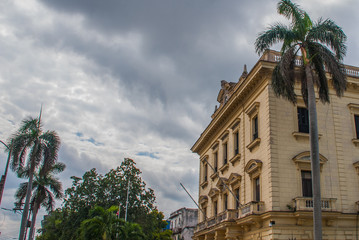 Classic building and palm trees on the background of a stormy sky. Havana. Cuba