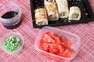 Sushi roll set, soy sauce, pickled ginger, wasabi in a disposable container on a napkin.