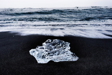 large ice rocks sitting in black sand on the shore