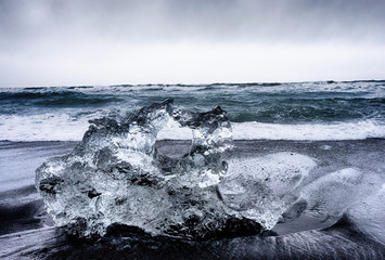 large ice rocks sitting in black sand on the shore