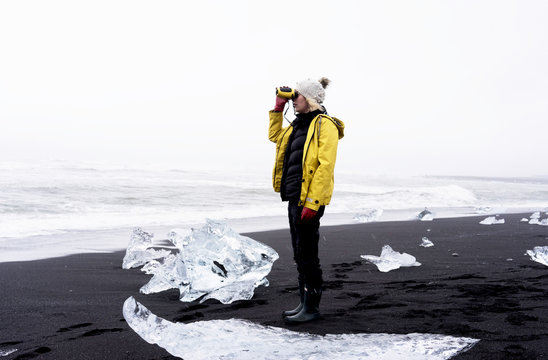 Woman standing between ice rocks with binoculars 