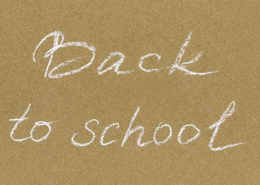 Hand drawn inscription white pastel crayon "Back to school" on the brown craft paper. Back to school background with title texts poster design