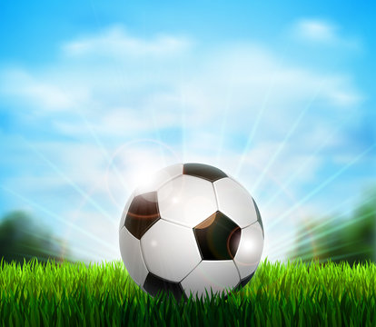 White and black soccer ball on the fresh green glade with grass. Background with blue sky, sunshine and sport equipment for playing football.