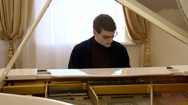 young pianist with glasses playing on a white grand piano