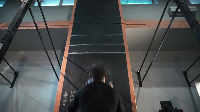 Back view of athletic man in black sportswear throwing weight ball in wall working out in gym.
