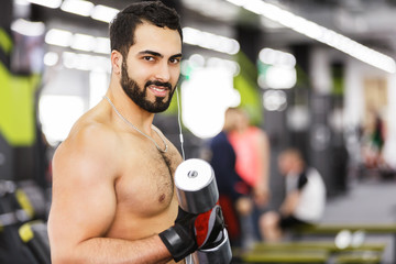 Topless bearded man holds metal dumbbell in the gym