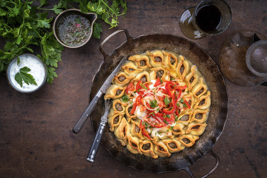 Traditional Armenian manti with mincemeat and paprika tomato salad as top view in a cast iron pan