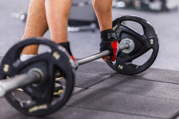 Fototapeta premium Man wears black gloves takes barbel in the gym