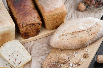 Different types of bread from the bakery, lie on a wooden oak board. Around walnuts and hazelnuts.