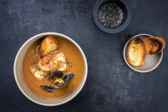 Traditional French fish soup with prawns and mussels as top view in a bowl