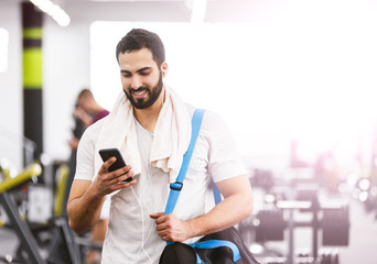 Muscular man walking in the gym holding smartphone