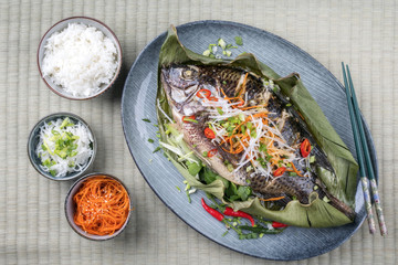 Traditional Thai barbecue tilapia fish with chili and vegetable as top view on a banana leaf