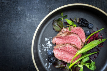 Traditional barbecue aged sliced fillet steak with wild garlic and fruits top view on a plate with...