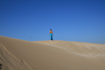 Fototapeta na wymiar Young woman in blue skirt in sand dunes