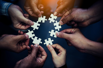 Businesspeople joining puzzle pieces in office. Hand holding piece of blank jigsaw puzzle with paper frame background.