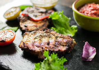 Grilled meat served with vegetables, spices on a slate plate.