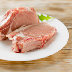 Raw pork brisket, ribs on a white plate on a wooden background.