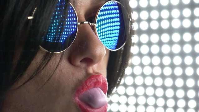 Hot brunette in round sunglasses, chewing gum and blowing a bubble. 4k, slow motion.