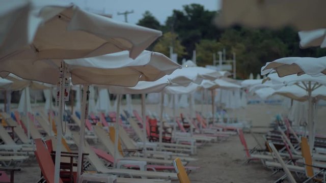 Slow motion shot of a wind waving sun umbrellas at the beach with the rows of empty sunbeds