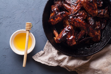 Chicken wings in thick barbecue sauce with garlic on black cast iron pan on gray rustic background.
