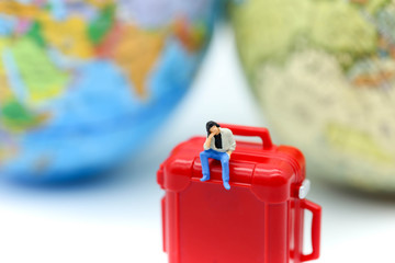 Miniature people : man sitting on red suitcase with mini global world,Adventure stories,Tourist planning vacation concept.