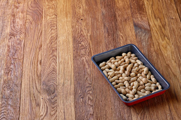 Unpeeled raw peanut on baking tray over wooden background, selective focus, shallow depth of field.