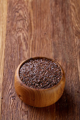 Flax seeds in wooden bowl on rustic wooden background, top view, selective focus