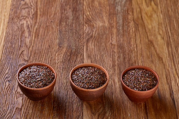Three ceramic bowls with flaxseeds arrenged in row over wooden background, top view, selective focus