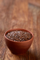 Flax seeds in ceramic bowl on rustic wooden background, top view, shallow depth of field